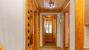 A wooden hallway with a rug, wooden walls, and a door leading to another room.