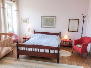 A bedroom with a wooden bed, a crib, a red chair, and a floor lamp. - Les Londes by Interhome (Bayeux)