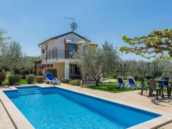 Une villa à deux étages dotée d’une piscine, d’un espace salon extérieur et d’oliviers.