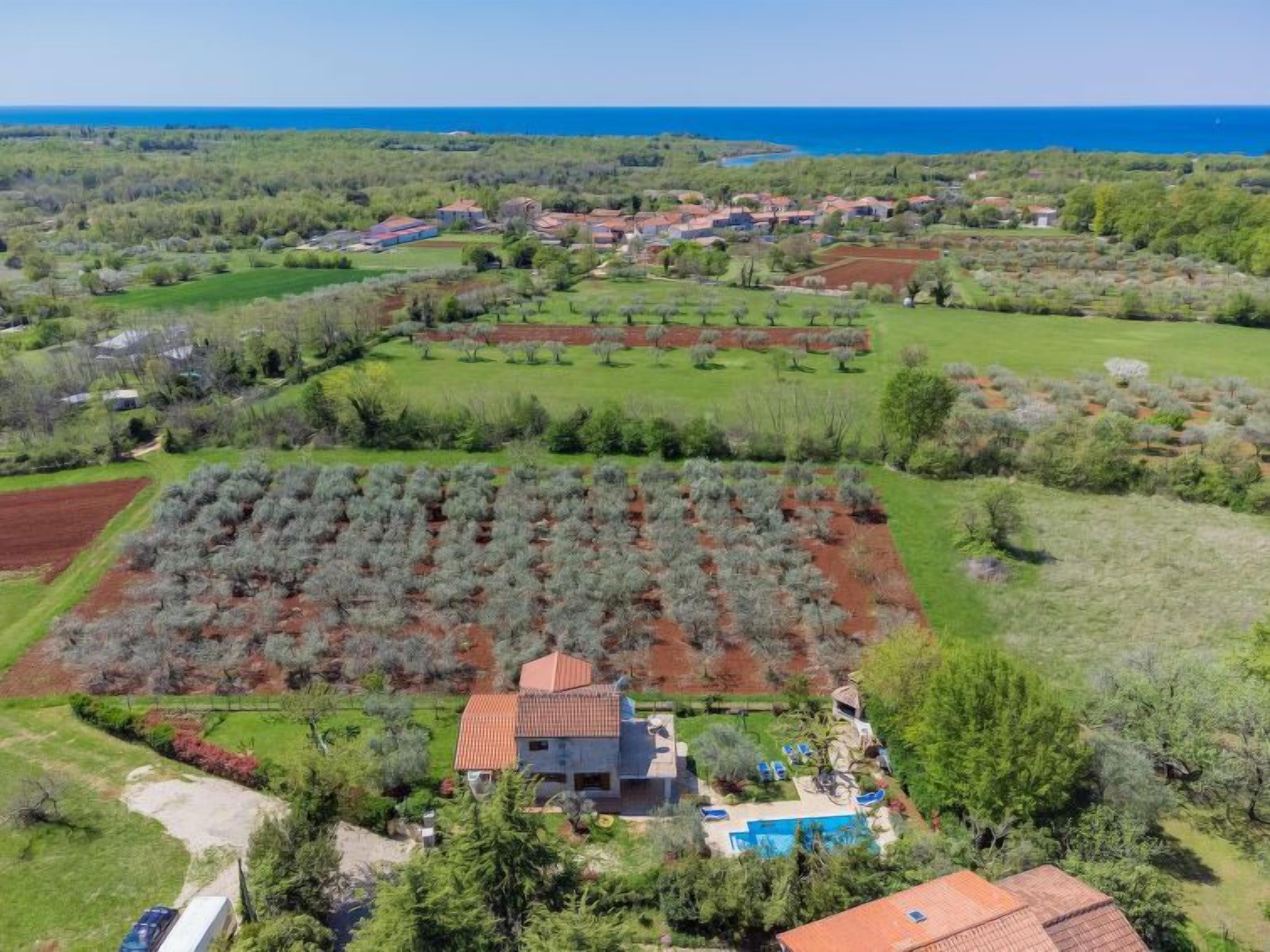 A coastal property with a swimming pool, a house with a red roof, and a view of the sea.
