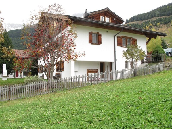 A white building with wooden shutters, a wooden fence, and a tree with red leaves in front. - Casa Posta Berther-Roth by Interhome (Rueras Dieni)