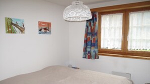 Ein Schlafzimmer mit einem großen Bett, einem Fenster mit Vorhängen und zwei an der Wand befestigten Bildern.