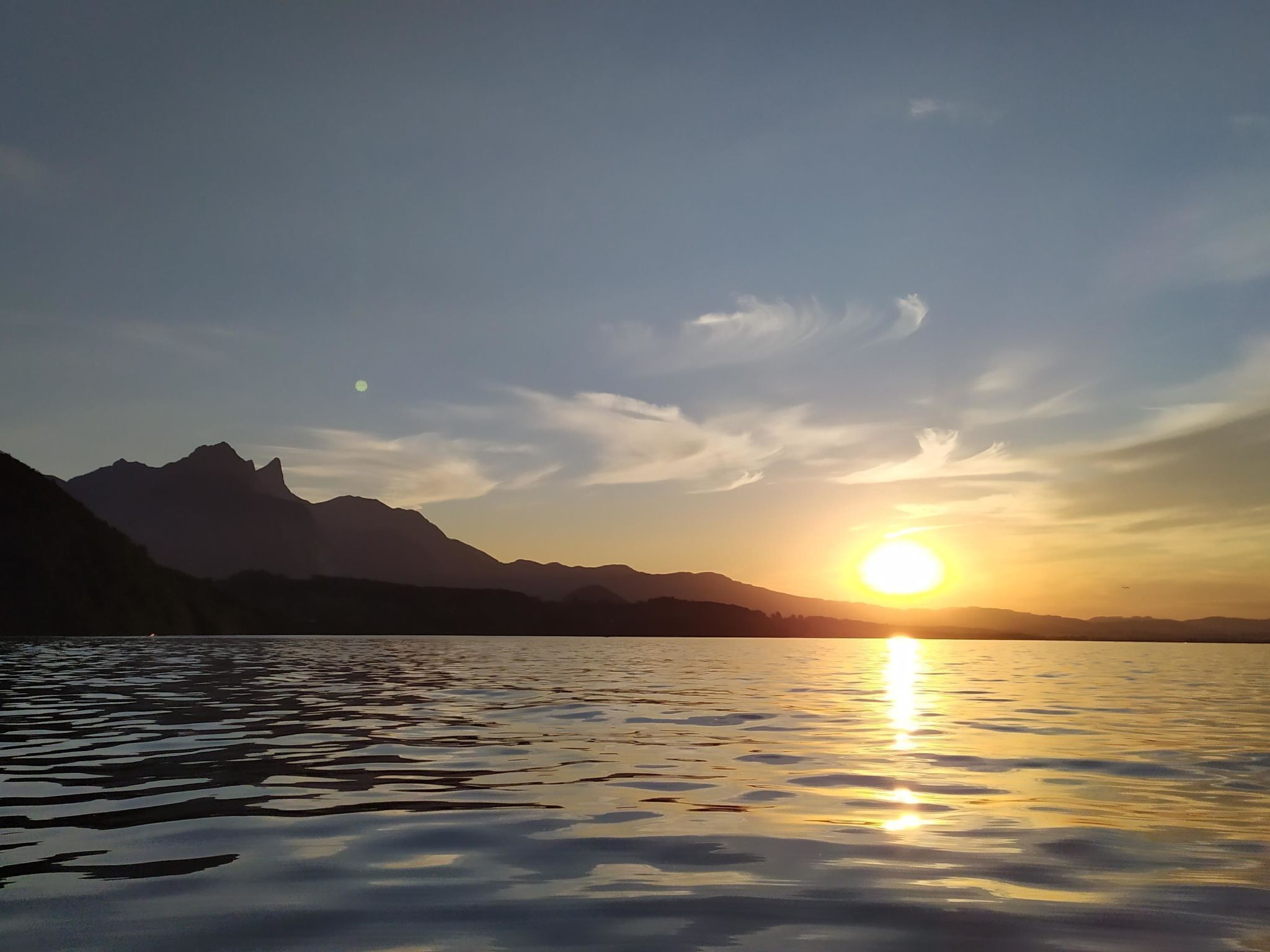 Ein Sonnenuntergang über einem stillen See mit Bergkonturen im Hintergrund.