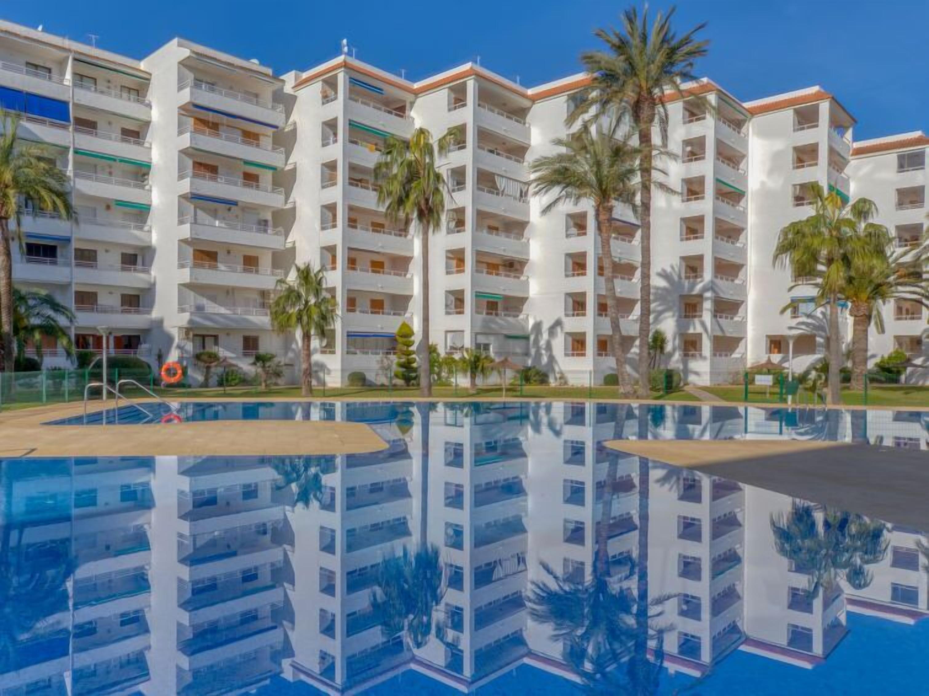A multi-story hotel with a central swimming pool, palm trees, and balconies.