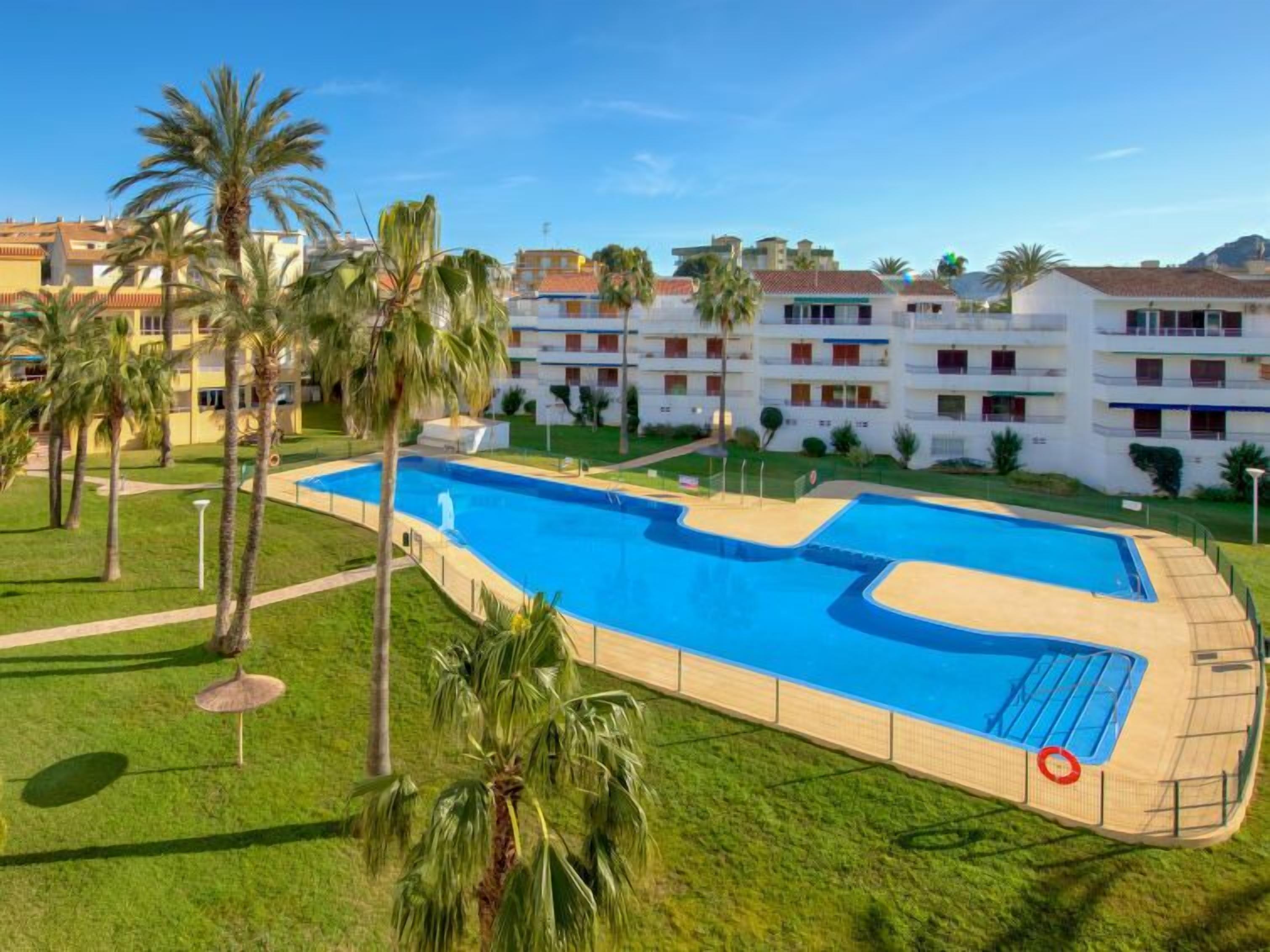 Une piscine entourée de palmiers et un bâtiment blanc doté de balcons.