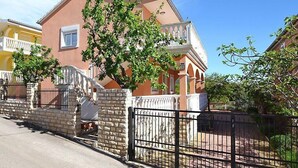Une maison à deux étages avec un balcon, un mur en pierre et un portail en métal.