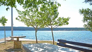 Un espace de pique-nique au bord du lac, avec une table en pierre, des bancs et des arbres.