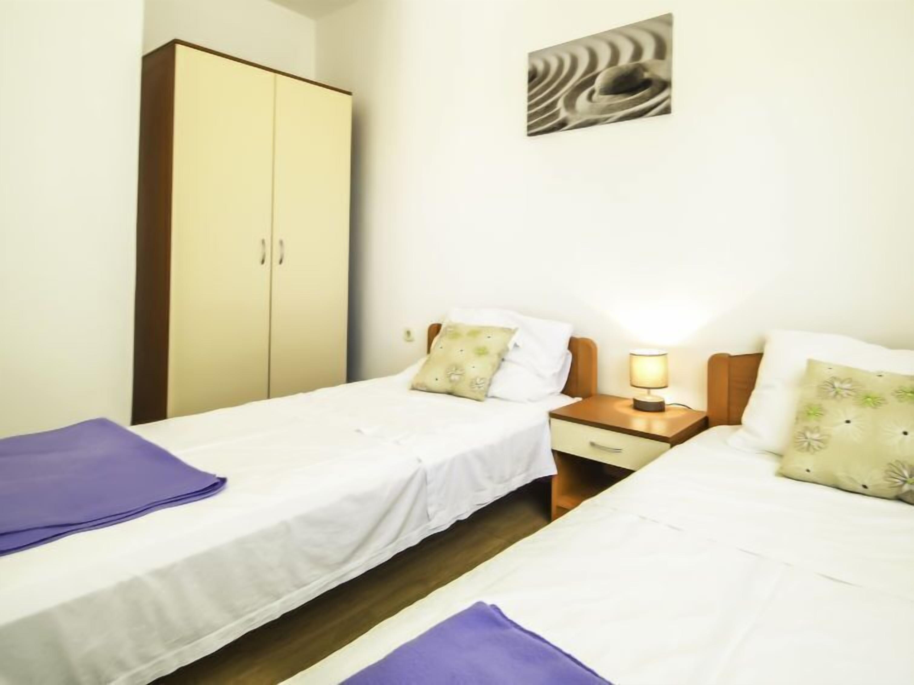 A twin room with two beds, a wardrobe, a nightstand with a lamp, and a wall-mounted artwork.