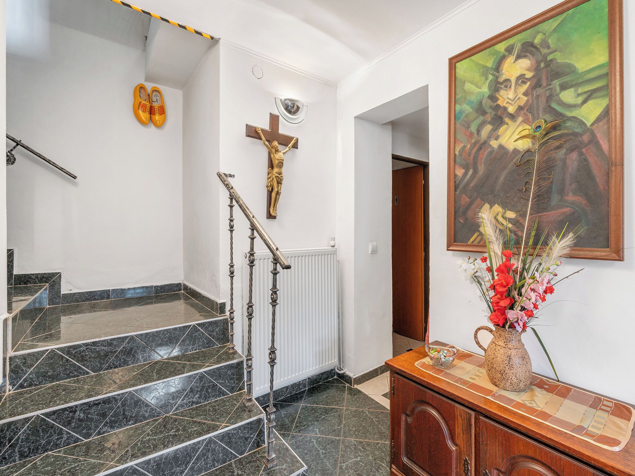 A staircase with a metal handrail, a crucifix, and a painting on the wall.