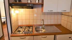 Eine kleine Küche mit Gasherd, Spüle und einem kleinen Kühlschrank. Oberhalb des Herdes befinden sich Schränke und ein Regal mit Küchenutensilien.