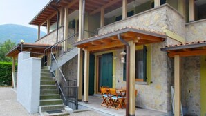 Ein zweistöckiges Steinhaus mit überdachter Außenbestuhlung und einer Treppe, die zu der oberen Etage führt.