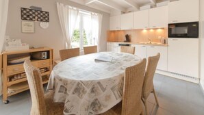 A modern kitchen with white cabinets, a microwave, and a dining area with a round table and wicker chairs.
