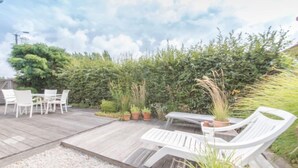 An outdoor patio with a wooden deck, white outdoor furniture, and potted plants.