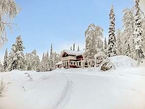 Et snedækket lodge med rødt ydre, omgivet af snebelastede træer og en klar himmel.