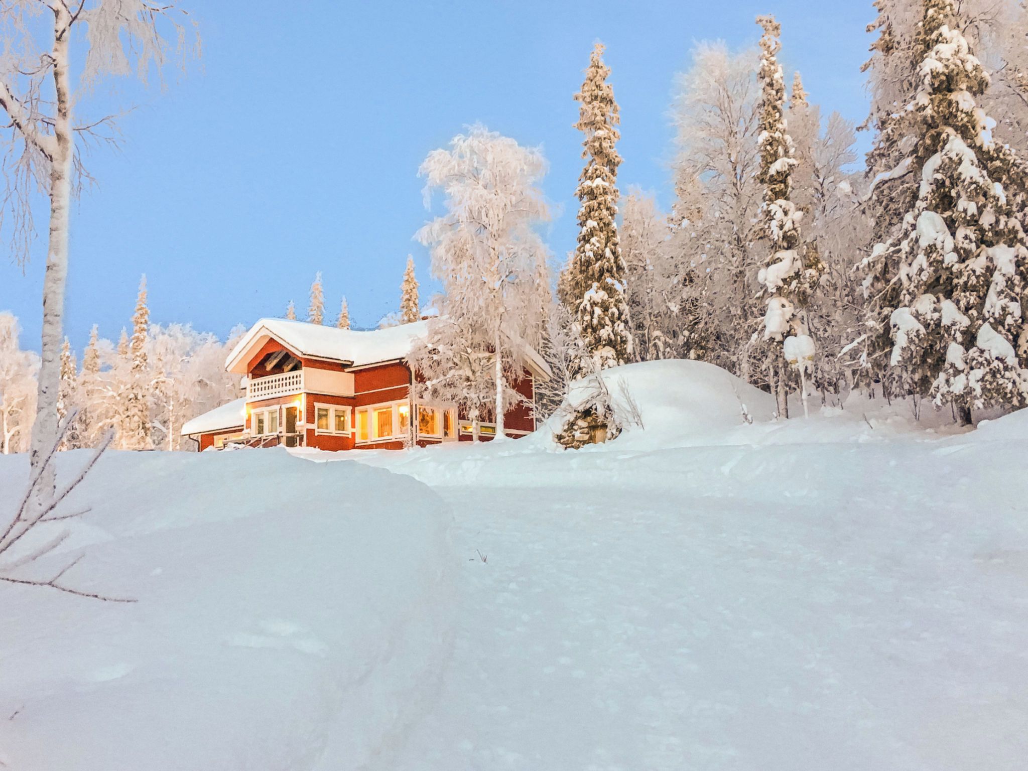 A snow-covered lodge with a balcony, surrounded by snow-laden trees.