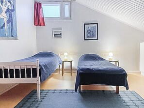 Et værelse med to enkeltsenge, en radiator, et vindue med gardiner og et billede i ramme på væggen.