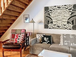 En stue med en trætrappe, en stribet sofa, en læderlænestol og et stort vægtæppe.