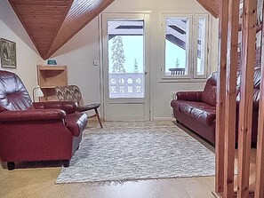 A living room with two leather sofas, a patterned rug, wooden ceiling beams, and a door with a frosted glass panel. - Pallaksen valkkorinne by Interhome (Enontekiö)