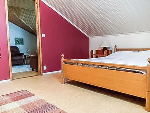 A bedroom with a wooden bed, a red wall, and a door leading to another room.