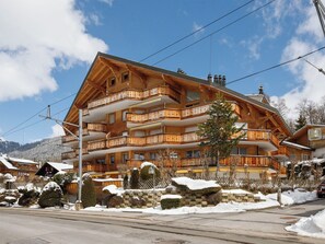 A multi-story wooden building with balconies, a stone wall, and snow-covered surroundings.