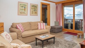 Una sala de estar acogedora con un sofá color beige, una mesa de centro y vistas a un paisaje montañoso a través de amplios ventanales.