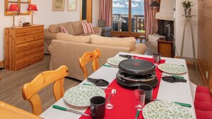 Una sala de estar acogedora con comedor, muebles de madera y vistas a montañas a través de un ventanal grande.