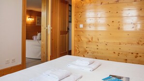 Habitación de hotel con pared de madera, cama con ropa blanca y baño visible a través de una puerta abierta.