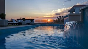 A swimming pool with a waterfall feature, lounge chairs, and a sunset view. - Melandura by Interhome (Pag/Dinjiška)