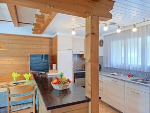 A modern kitchen with wooden beams, a fruit basket on the counter, and a TV in the background.