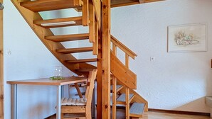 En trätrappa med en stol och ett bord, en tavla på väggen och en vit vägg med en tydlig struktur.