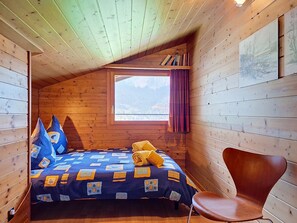 A cozy cabin room with a bed, a chair, a window, and a bookshelf.