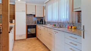 Ett modernt kök med bänkskivor i granit, en inbyggd ugn och ett fönster med tunna, genomskinliga gardiner.