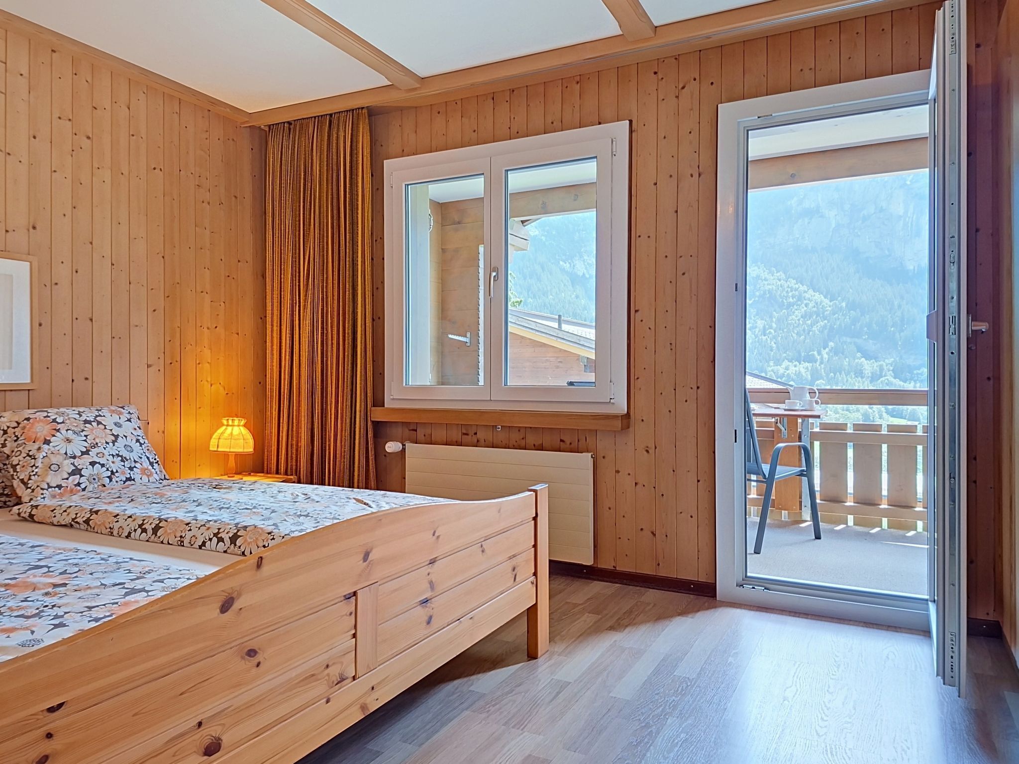 A wooden bedroom with a bed, a window, and a view of a balcony.
