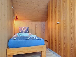 A small, cozy bedroom with a wooden bed, a nightstand, and a red lamp.