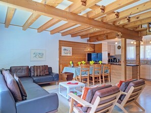 A cozy living area with a sofa, chairs, a dining table, and a kitchen in the background.