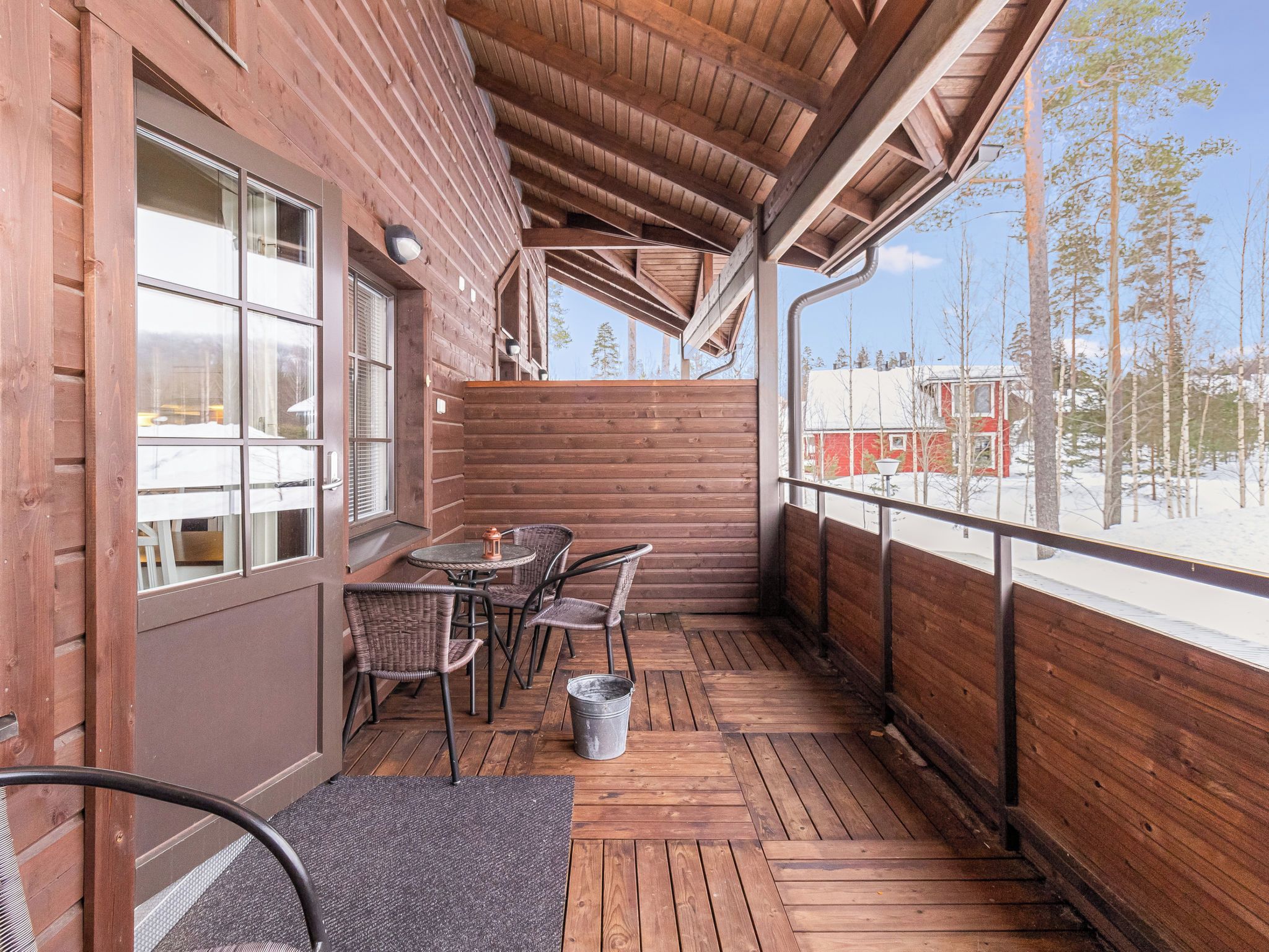 A wooden deck with a table and chairs, a metal bucket, and a view of a snowy landscape.