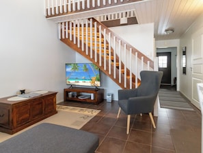 Una sala de estar con una escalera de madera, un televisor, un sillón gris y un aparador de madera.