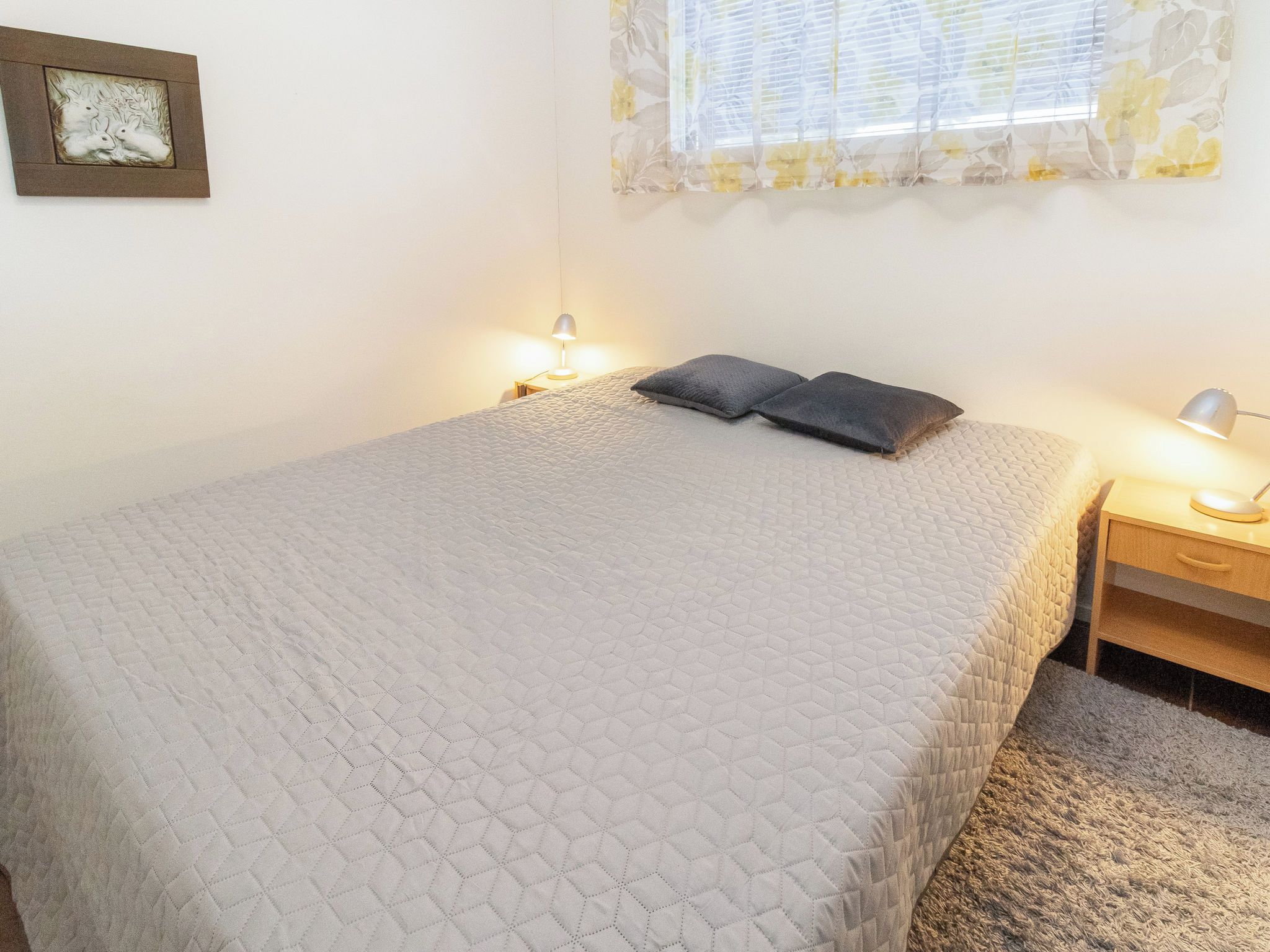 Ein ordentlich bezogenes Bett mit einer gesteppten Decke, zwei Kissen und Nachttischlampen.