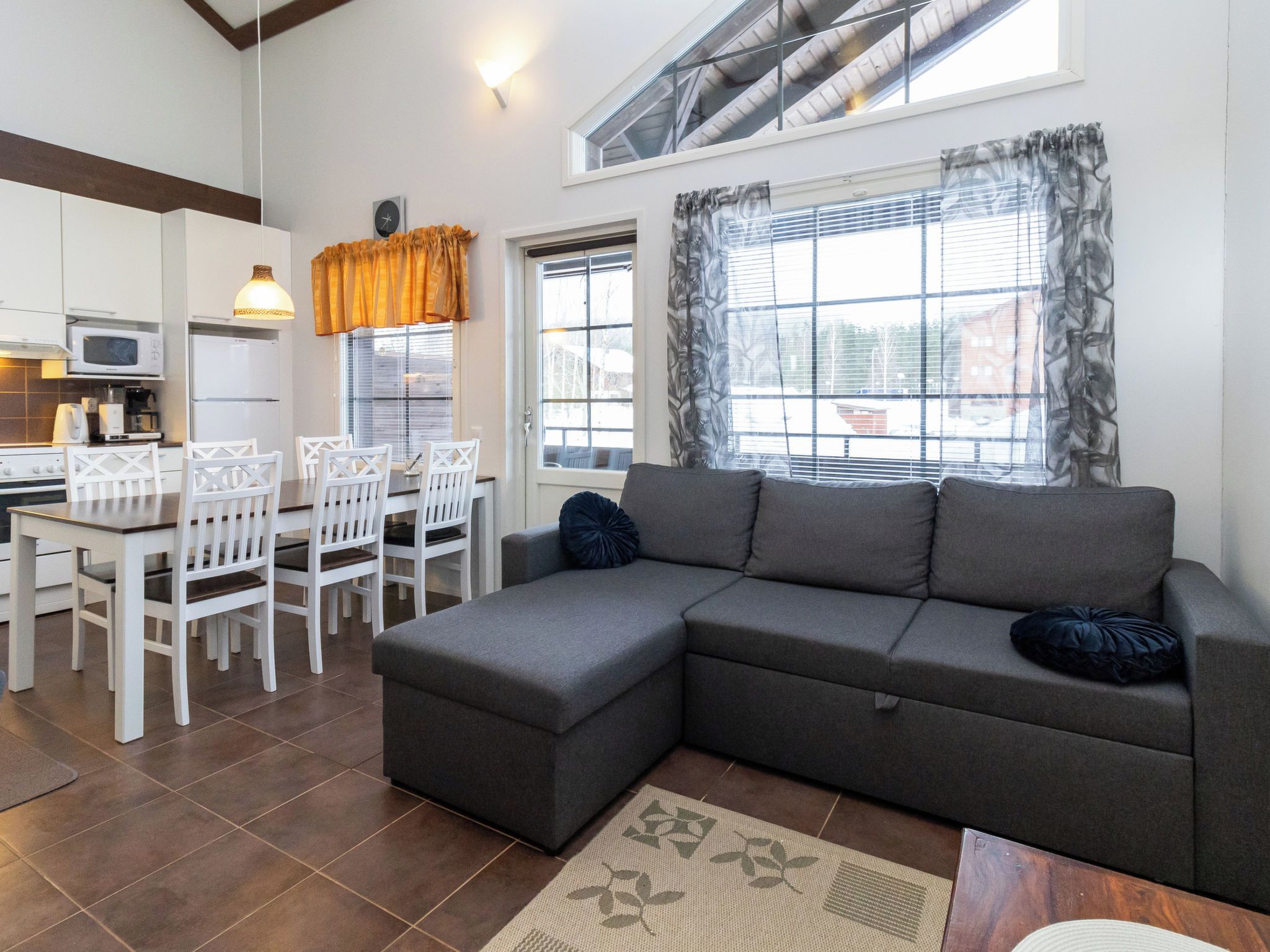 Een moderne woonkamer met een grijze modulaire bank, een eettafel met witte stoelen, en een keuken met witte kasten en apparatuur.