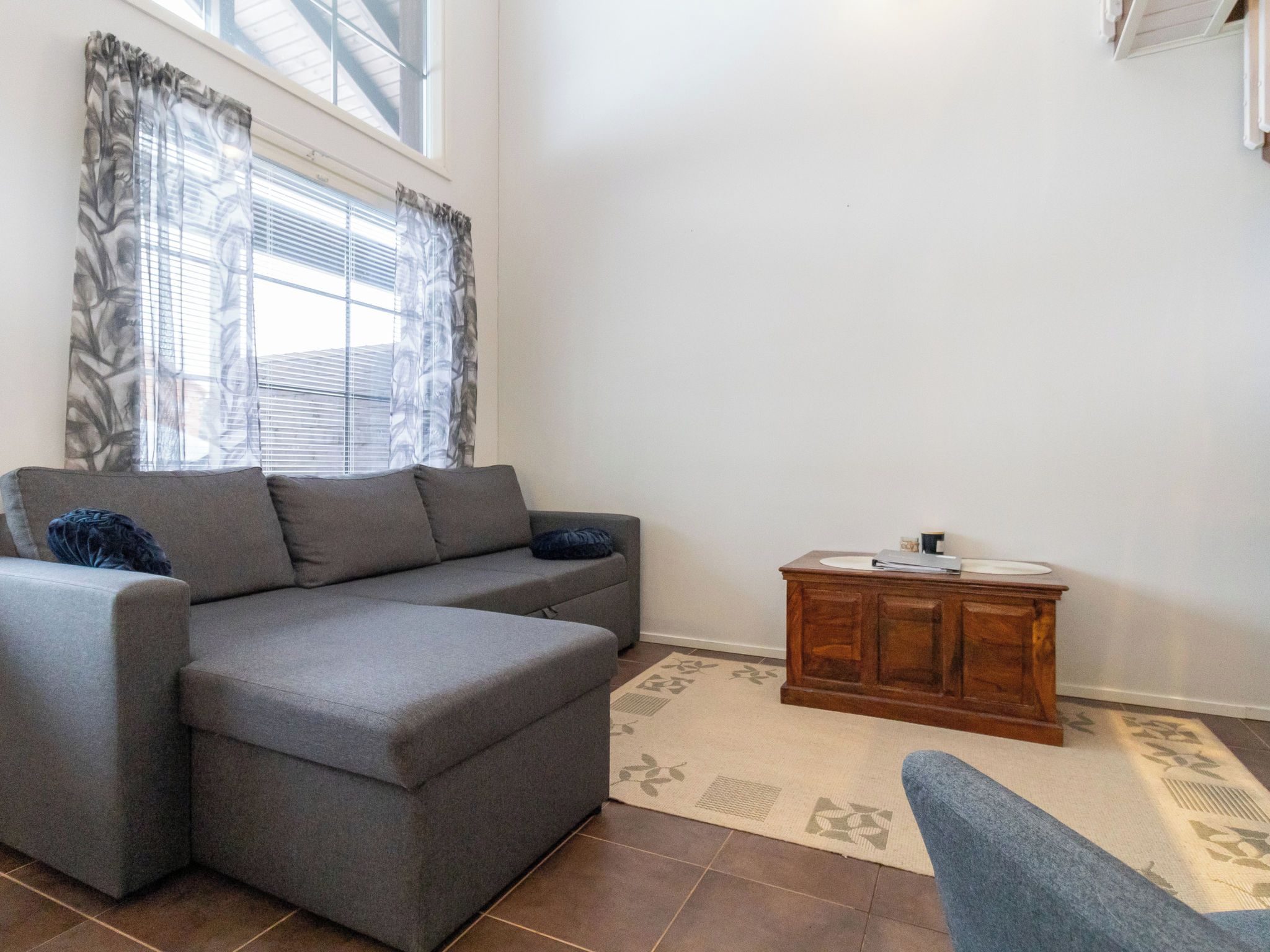 A living room with a grey sectional sofa, a wooden side table, and a window with patterned curtains.