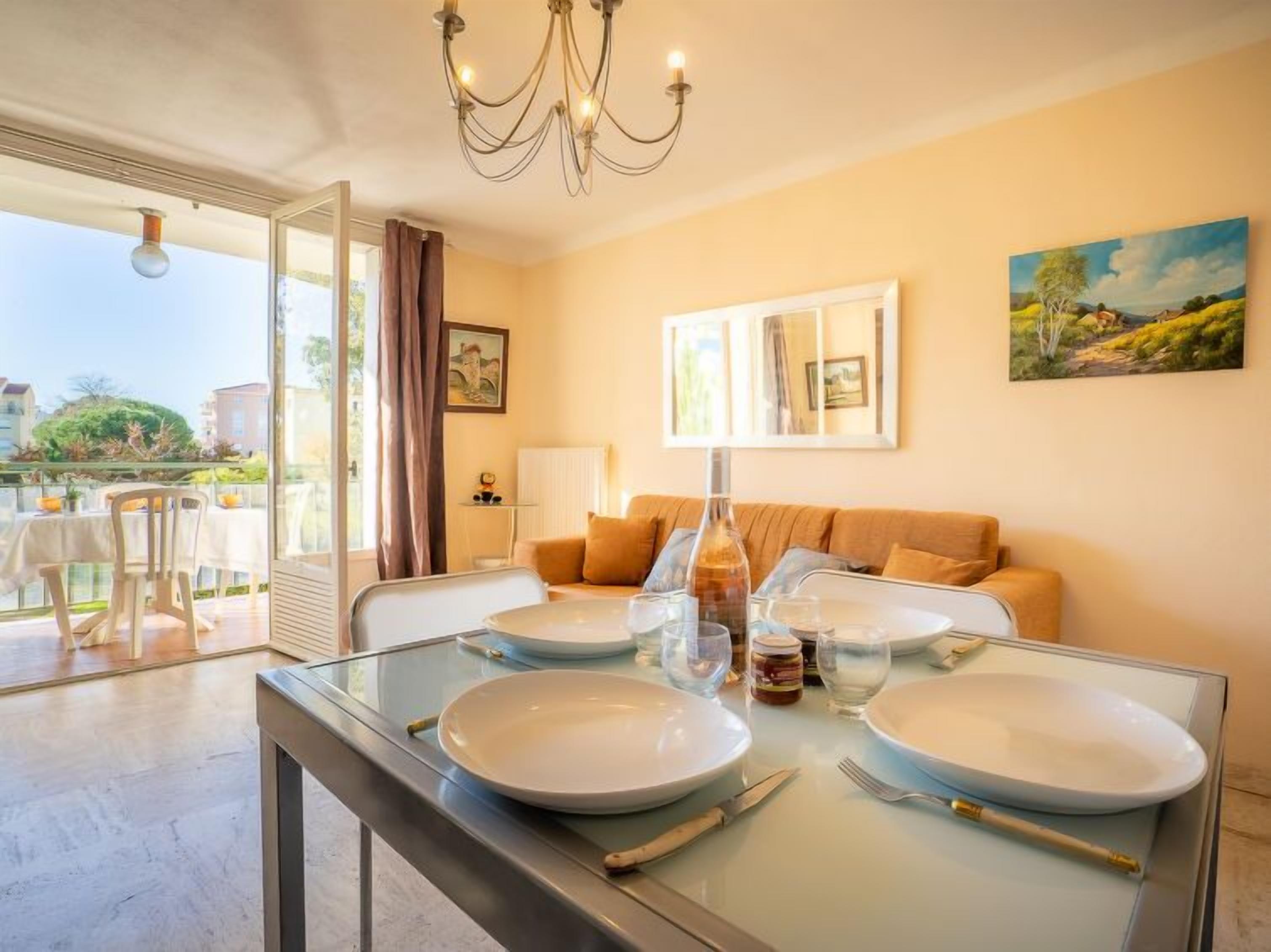 Uma sala de jantar com uma mesa de vidro posta para quatro pessoas, um sofá e um quadro na parede.