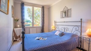 Une chambre à coucher avec un grand lit, une table de chevet avec une lampe, une fenêtre avec des rideaux et un miroir fixé au mur.