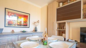 Un coin repas avec une table dressée pour quatre personnes, un tableau accroché au mur et un meuble en bois contenant des ustensiles de cuisine.