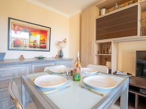 A dining area with a table set for four, a painting on the wall, and a wooden cabinet with kitchen items.