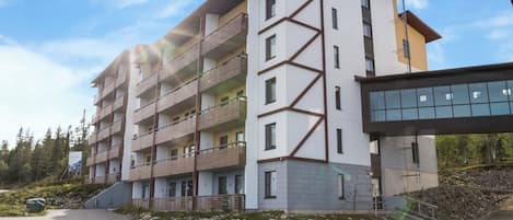 Un immeuble à plusieurs étages doté de balcons, d’un espace de stationnement et intégré dans un paysage naturel.