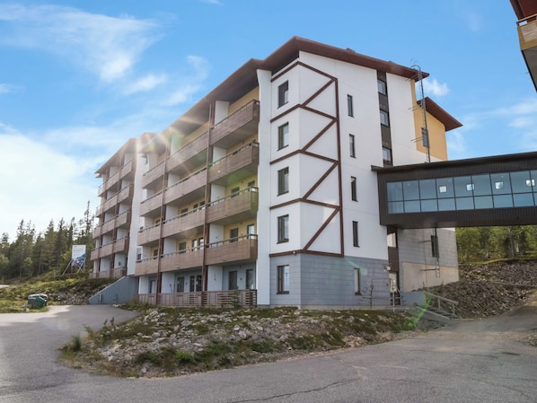 A multi-story building with balconies, a parking area, and a natural landscape.