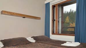 A bedroom with a bed, a window with curtains, and a wall-mounted light fixture.