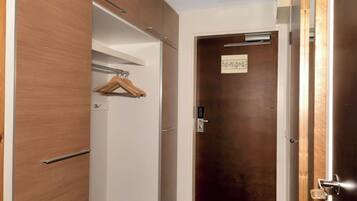 A room with a wooden wardrobe, a hanging coat rack, and a closed door with a lock.