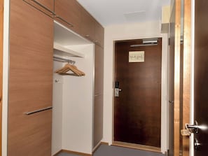 A room with a wooden wardrobe, a hanging coat rack, and a closed door with a lock.