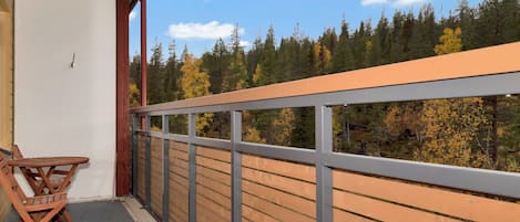 Ein Balkon mit Holzgeländer, Tisch und Stühlen mit Blick auf ein bewaldetes Gebiet.